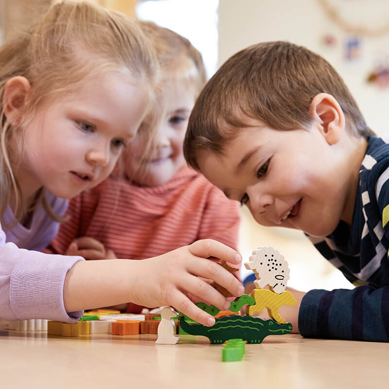 Three kids gathered around a table playing HABA Animal Upon Animal